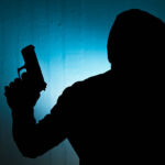 Silhouetted man with gun against blue wall background