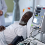 African american male patient lying on hospital bed next to blood pressure monitor
