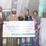 Cheluchi winner of NNLG NPL 2021 displaying her plaque and dummy cheque with organisers of the competition