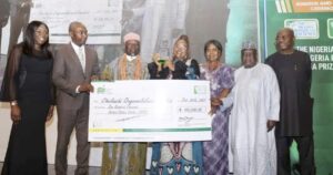 Cheluchi winner of NNLG NPL 2021 displaying her plaque and dummy cheque with organisers of the competition