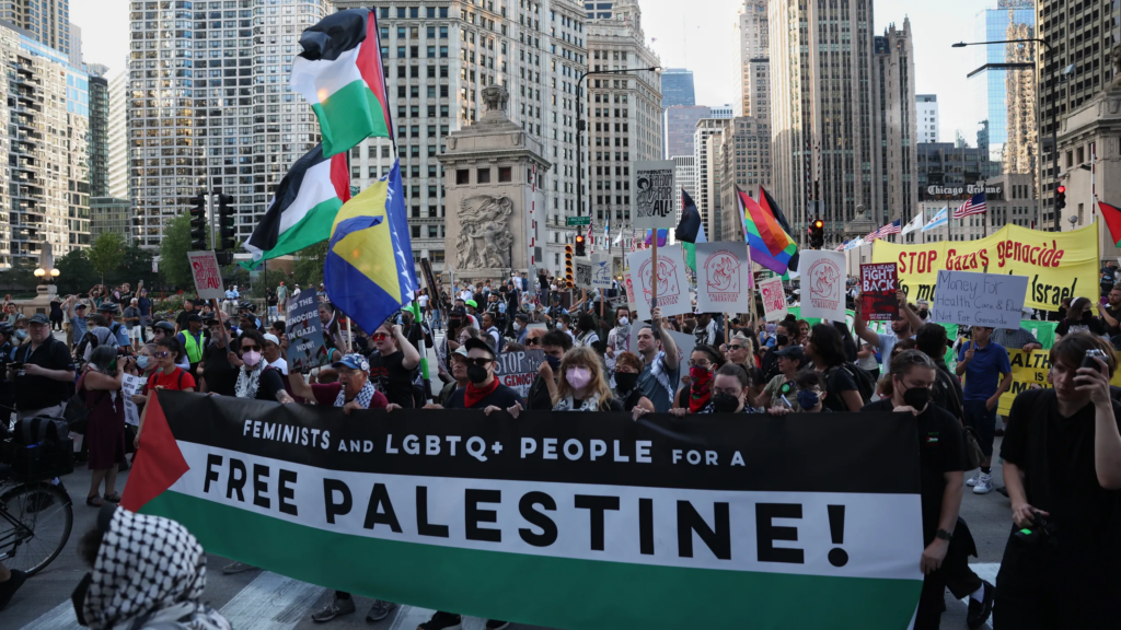A large crowd of protesters holding signs and Palestinian flags marching