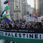 A large crowd of protesters holding signs and Palestinian flags marching