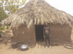 Uguru standing in front of his hut