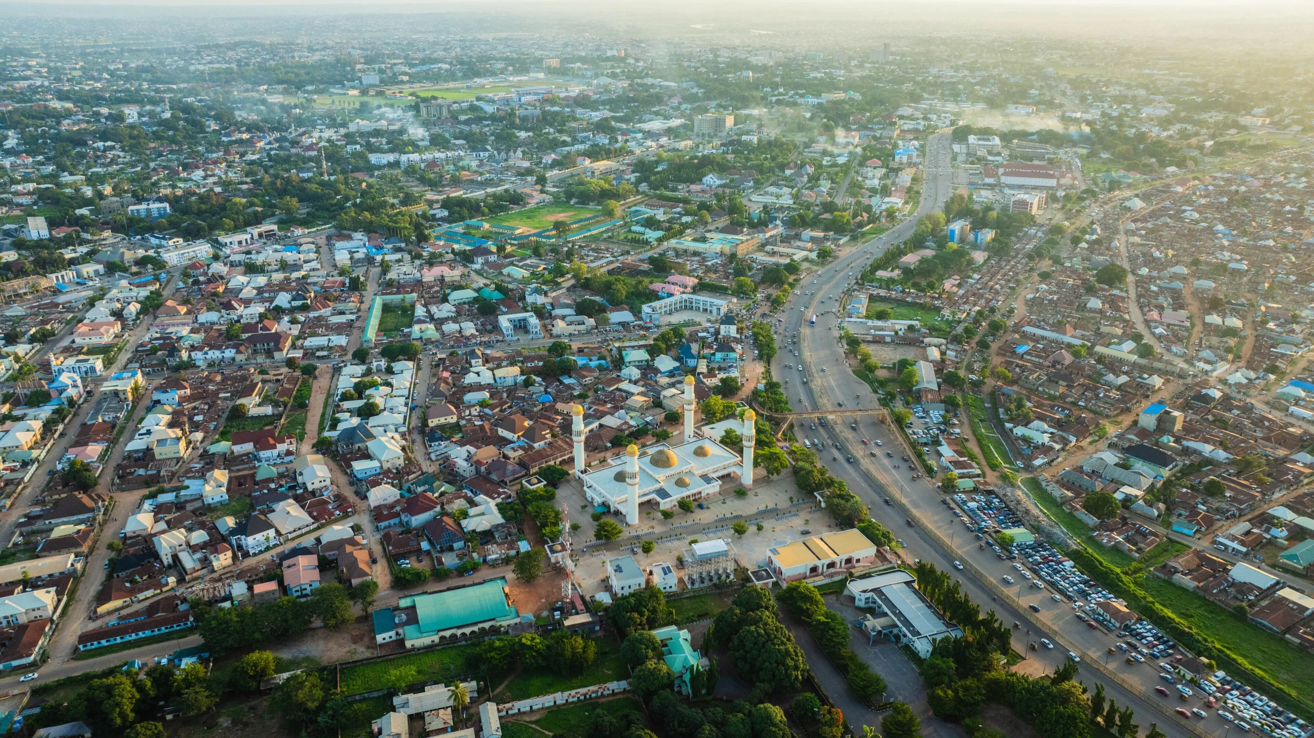 Aerial view of the magnificent mosque gleaming under the sun’s embrace, contrasting with the surrounding urban tapestry, Ungwan Sarki, Kaduna, Nigeria