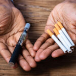 hands-holding-a-vape-pen-and-cigarettes