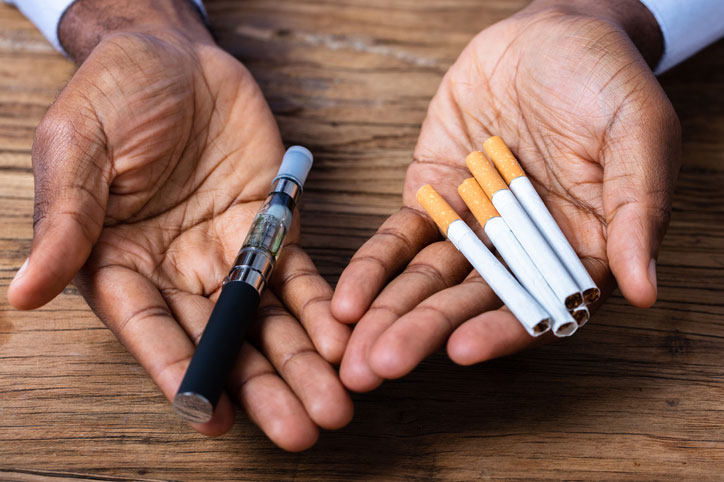 hands-holding-a-vape-pen-and-cigarettes